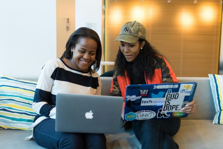 Two women engaged in collaborative work on laptops in a contemporary office setting.
